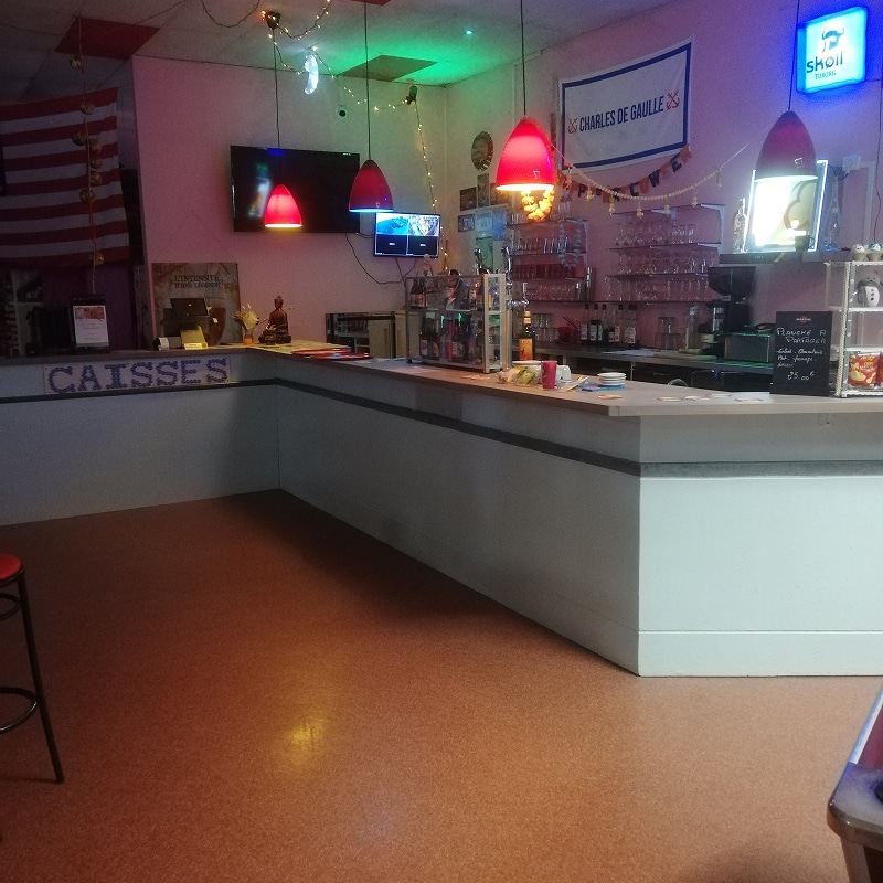Bar coloré avec long comptoir, écrans, néons rouges et verts. Textes 'CAISSES', 'CHARLES DE GAULLE', 'SKOLL', 'Planche Apéro 25€'.