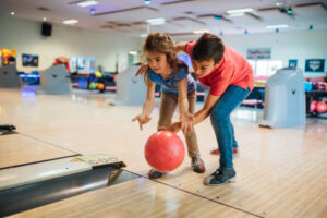 Sister teaching brother how to bowl