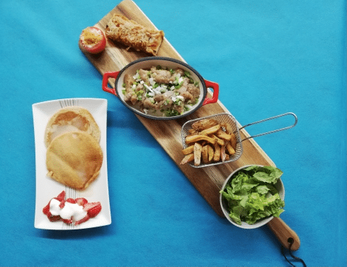 Délicieux Brunch Complet: Poulet, Frites, Pancakes, Salade Repas complet sur planche en bois: pancakes, fraises, viande, frites, salade, tomate farcie et pâtisserie frite sur fond bleu.