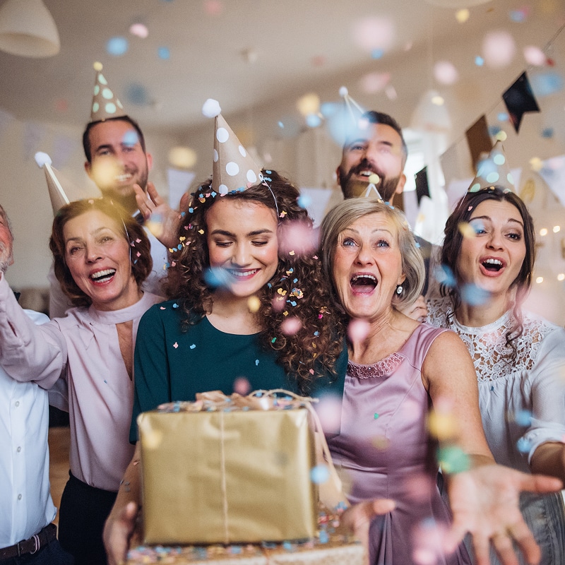 Fête d'anniversaire joyeuse : famille et amis célèbrent ! Groupe joyeux célébrant un anniversaire avec des chapeaux de fête et des confettis. Une femme tient des cadeaux, les autres rient de joie.