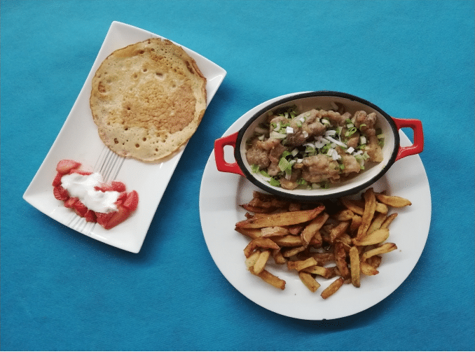Repas sur nappe bleue : une crêpe avec fraises et crème, un plat de viande en sauce aux oignons verts, accompagné de frites maison.