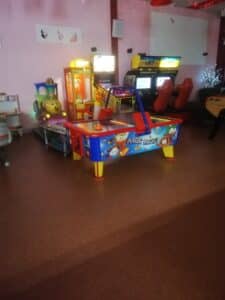 Salle d'arcade lumineuse avec table Air Hockey Magic, jeux vidéo de course 007, machine à griffes et manège enfant train souriant. Décorations murales Marilyn Monroe.