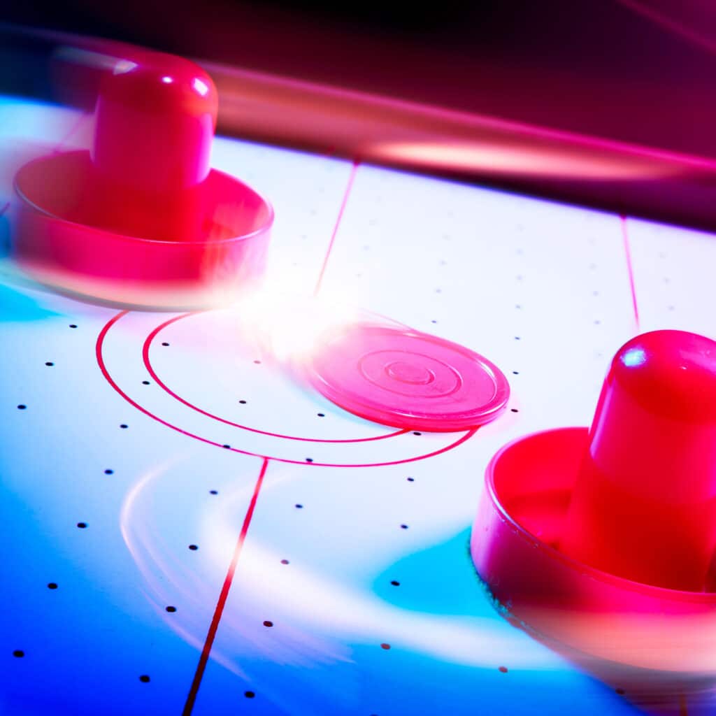 Table de air hockey avec deux maillets et un palet rouge vif, éclairés par une lumière intense, créant une ambiance dynamique.